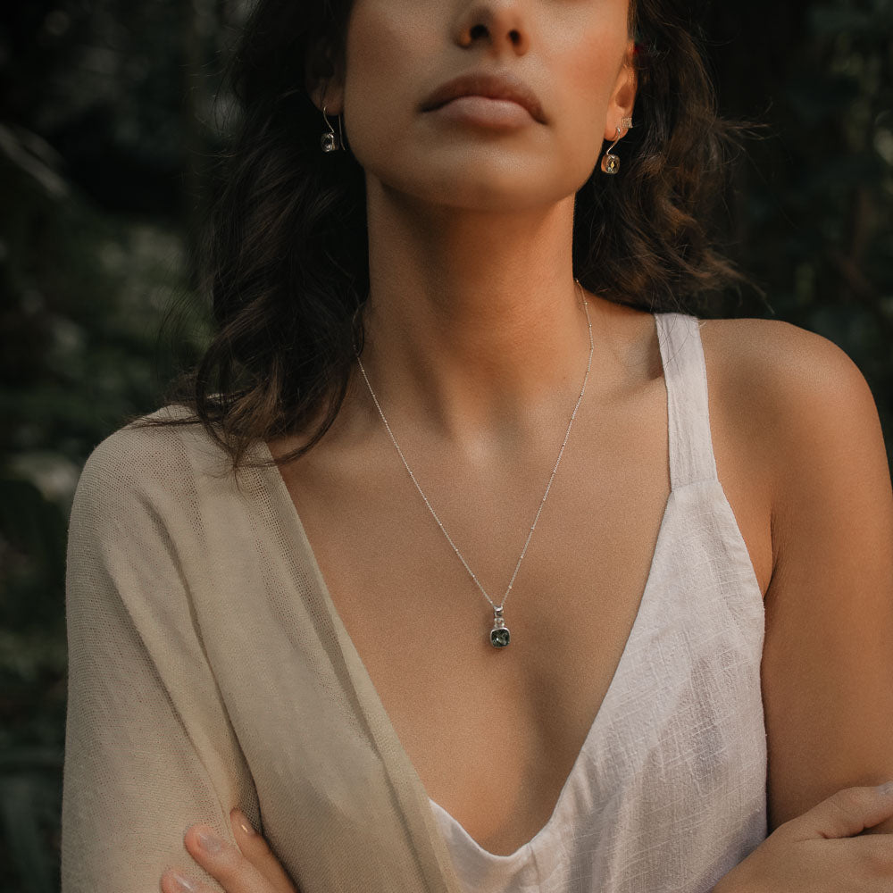 a woman wearing a pair of green amethyst square faceted earrings and pendant in white linen clothes