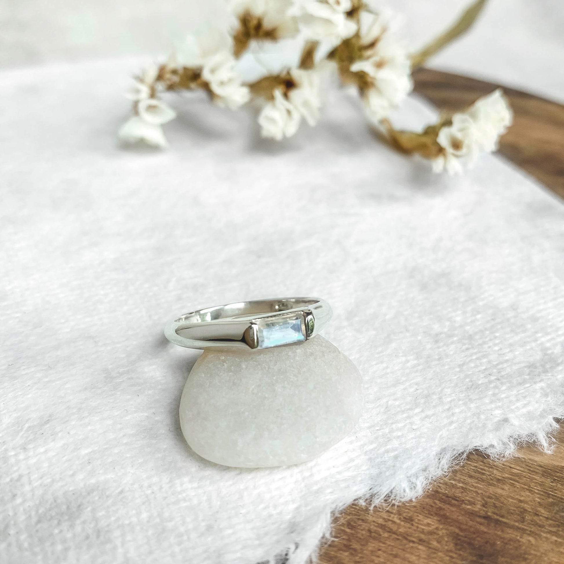 midi baguette moonstone silver ring resting on a smooth stone flower in background