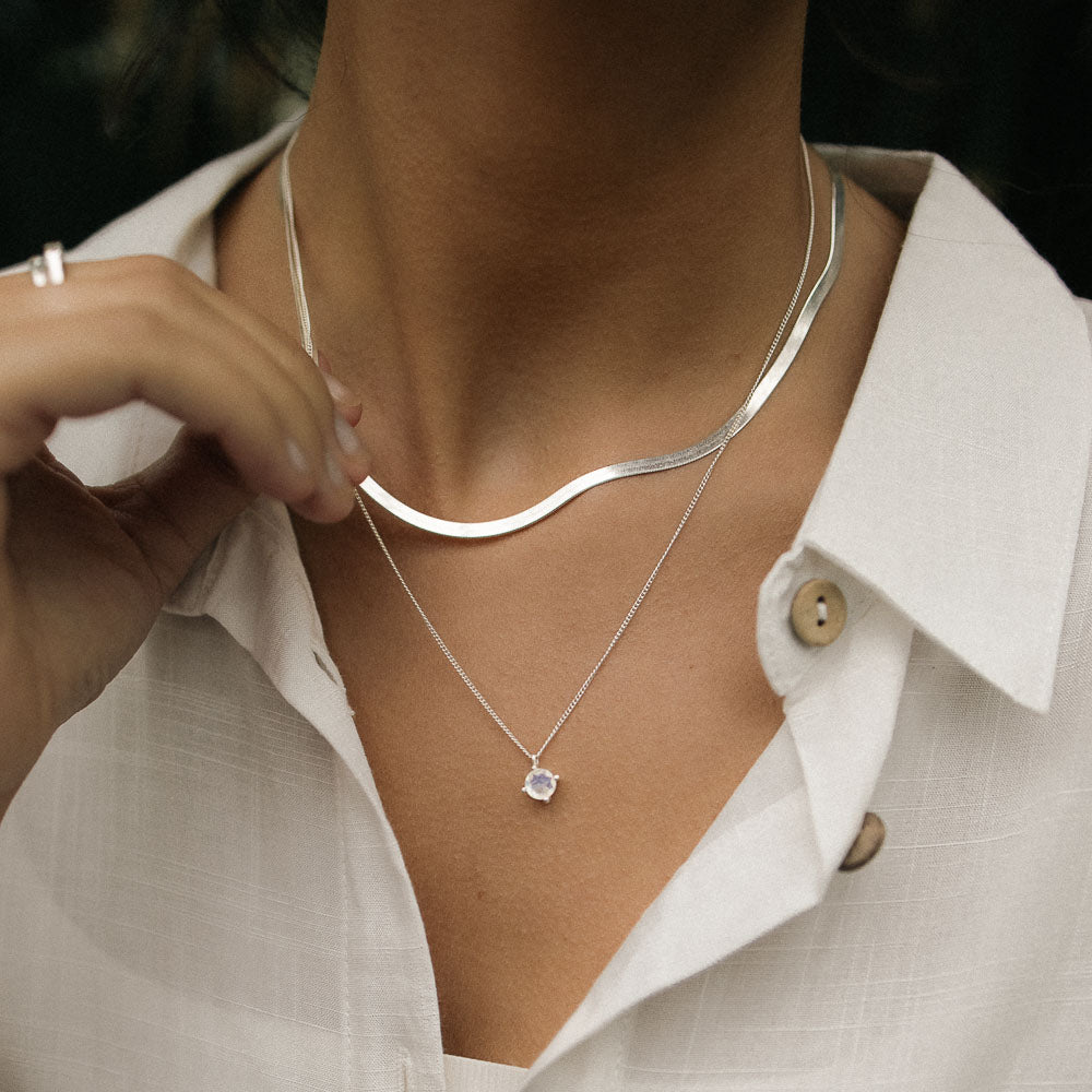 a woman wearing silver round moonstone necklace in a jungle with a white shirt on