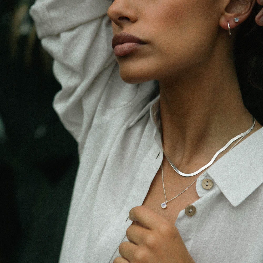 a woman wearing silver round moonstone necklace in a jungle with a white shirt on and her arms up