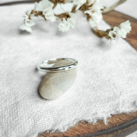 one silver solitaire moonstone ring resting on a smooth stone with blue colour