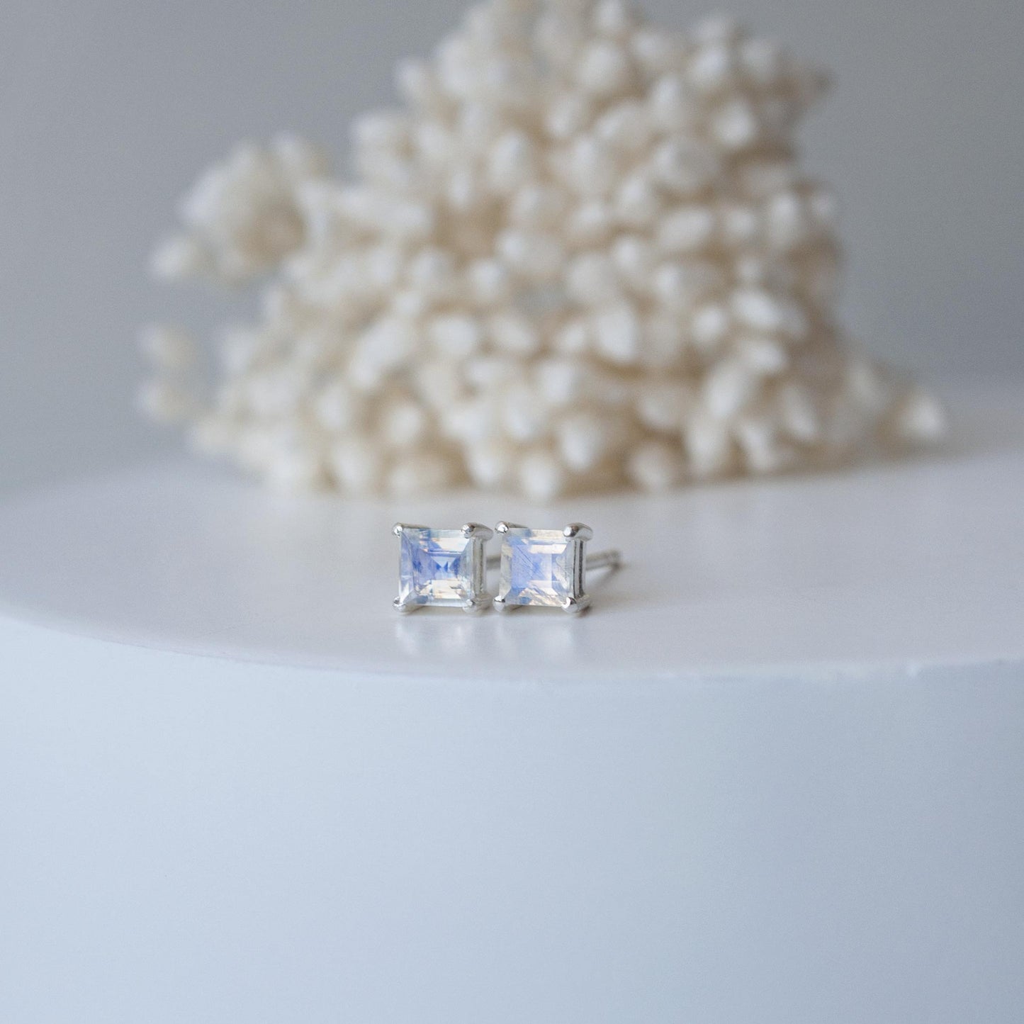 square moonstone studs on white shelf with flowers in the background