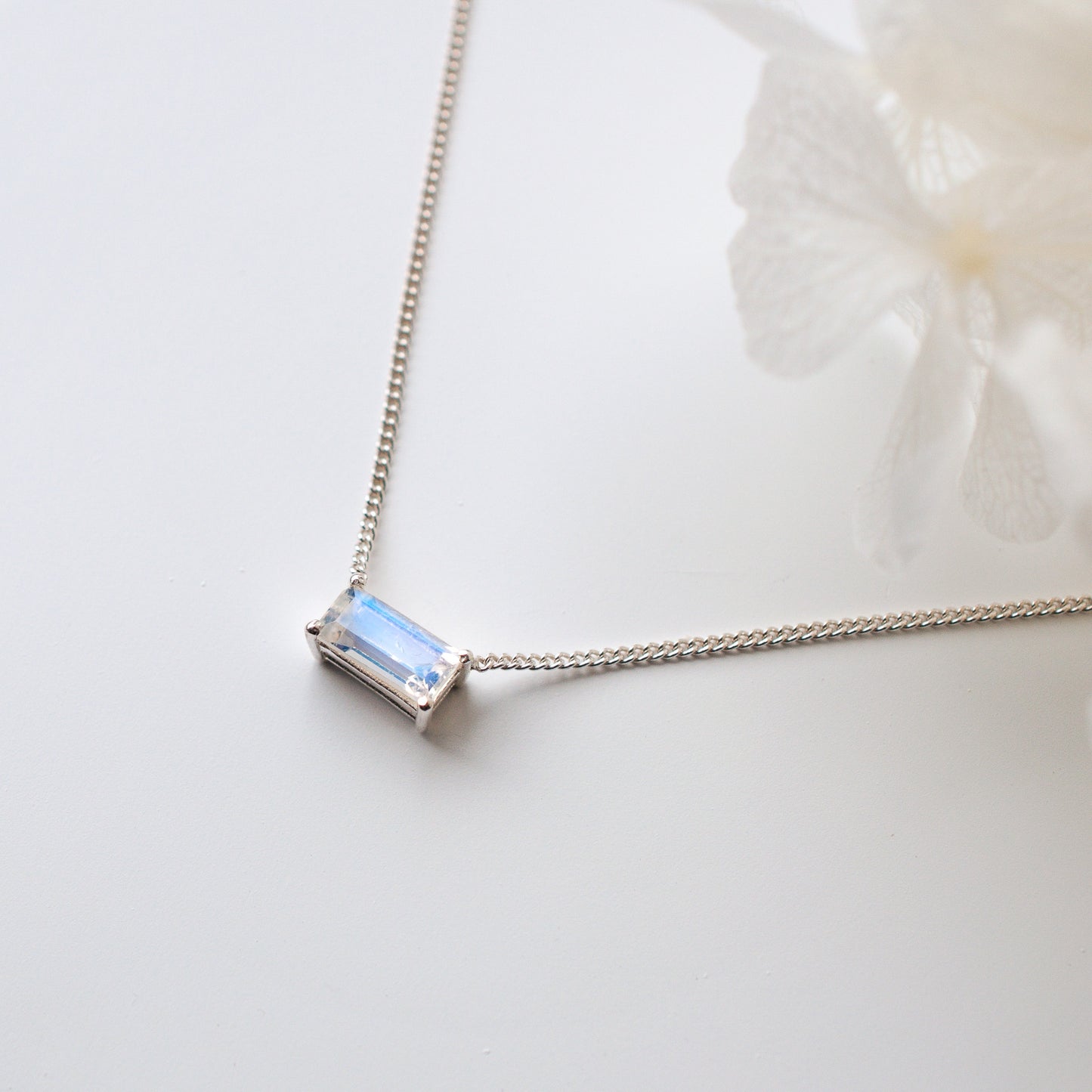 horizontal baguette rainbow moonstone pendant necklace with fine silver chain and flower on white surface