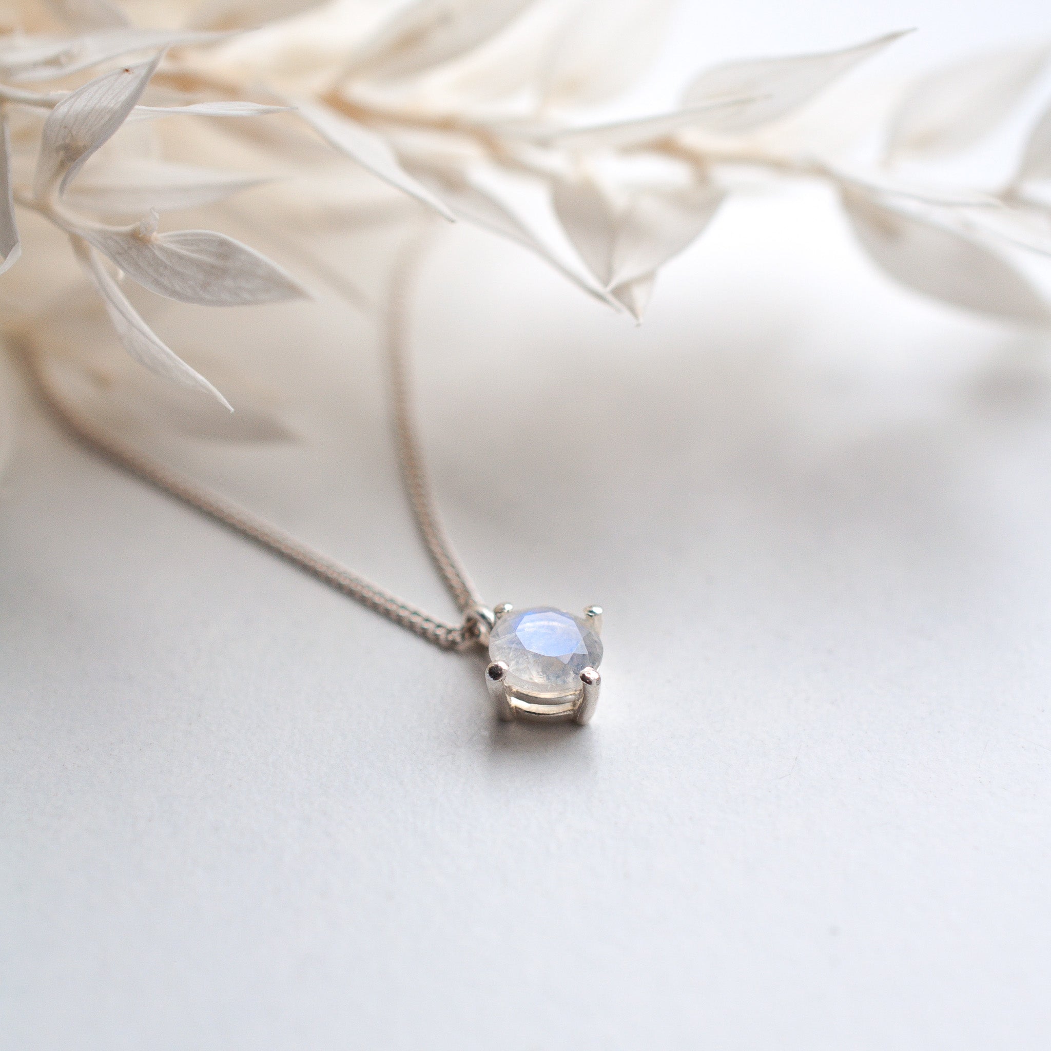 round faceted rainbow moonstone pendant necklace on white surface with preserved flowers